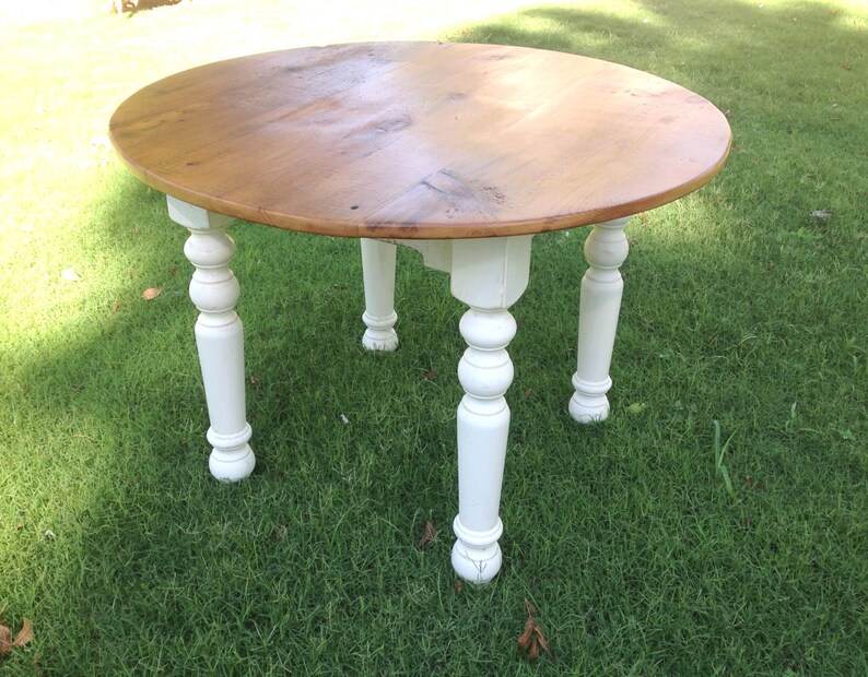 May include: A round wooden table with a natural wood top and white painted legs. The table has a simple, farmhouse style.