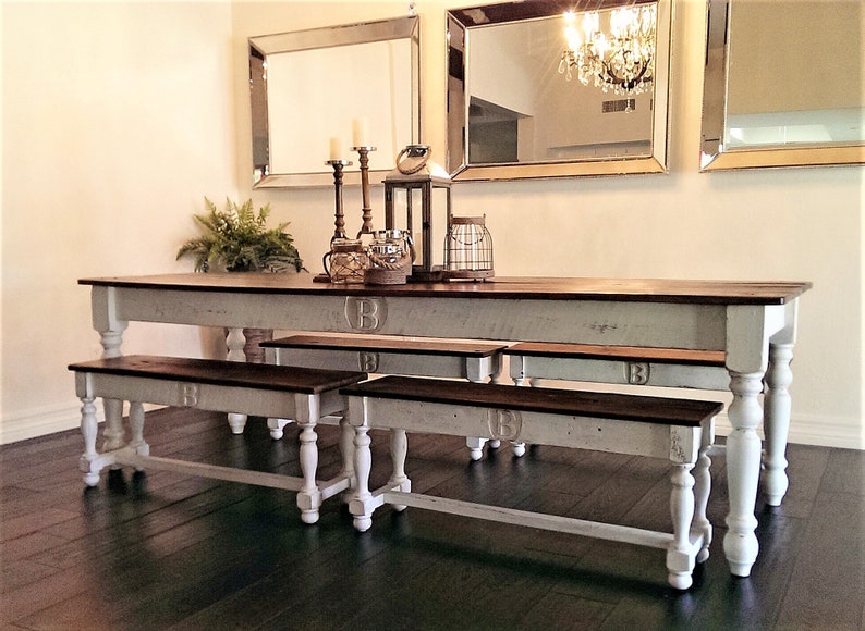 May include: White farmhouse style dining table with three matching benches. The table and benches have a distressed white finish with a dark wood top. The table and benches have turned legs and are decorated with a letter "B" on the top.