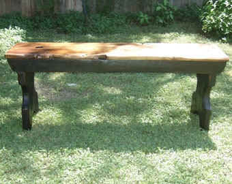 May include: A rustic wooden bench with a natural wood top and black painted legs. The bench is sitting on a grassy lawn.