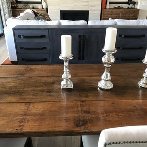 Pode incluir: Tr&ecirc;s casti&ccedil;ais de prata com velas brancas sobre uma mesa de madeira. A mesa &eacute; feita de t&aacute;buas de madeira recuperadas.