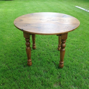 May include: A round wooden table with a natural wood finish and turned legs. The table is sitting on a green grassy lawn.