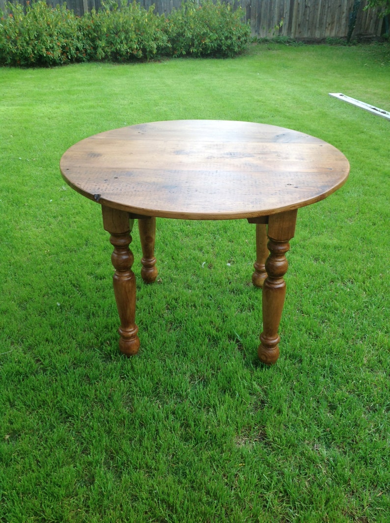 May include: A round wooden table with a natural wood finish and turned legs. The table is sitting on a green grassy lawn.