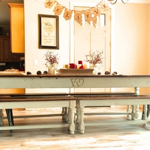 May include: A white farmhouse style dining table with two matching benches. The table has a distressed white finish and a dark wood top. The table is decorated with a red and gold centerpiece and a banner that reads "Believe".