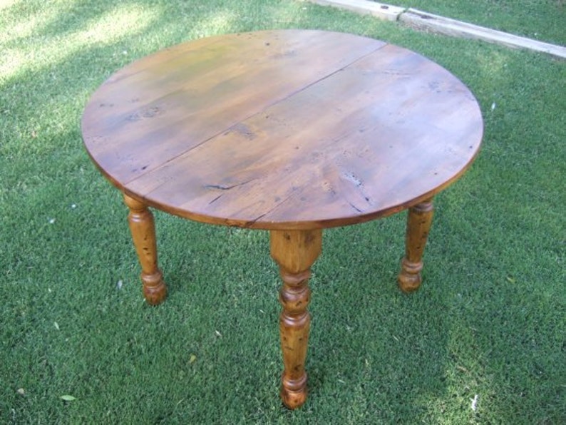 May include: A round wooden table with a natural wood finish and turned legs. The table is made of solid wood and has a rustic look.