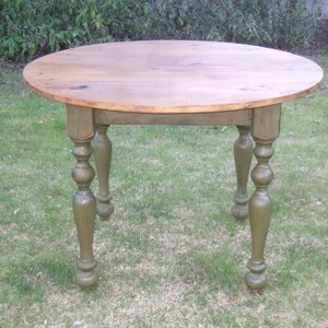 May include: A round wooden table with a natural wood top and green painted legs. The legs have a turned design with a ball at the bottom.