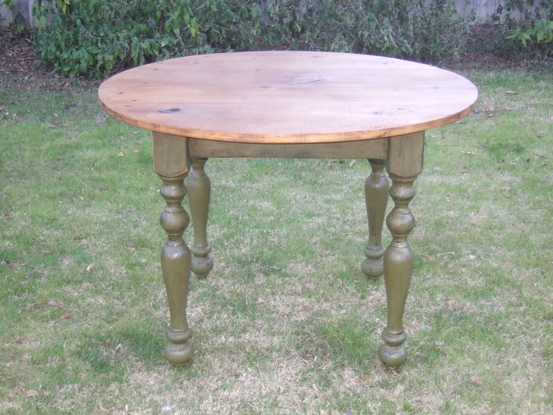 May include: A round wooden table with a natural wood top and green painted legs. The legs have a turned design with a ball at the bottom.
