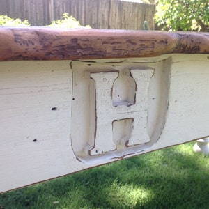 May include: Close-up of a white painted wooden table top with a large, white painted letter "H" carved into the surface. The table top has a distressed, rustic look.