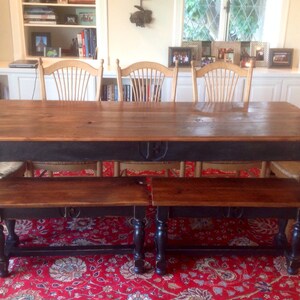 May include: A dark wood dining table with a black painted base and turned legs. The table is set with two benches with black painted bases and turned legs. The table and benches are on a red patterned rug.