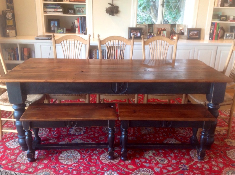 May include: A dark wood dining table with a black painted base and turned legs. The table is set with two benches with black painted bases and turned legs. The table and benches are on a red patterned rug.