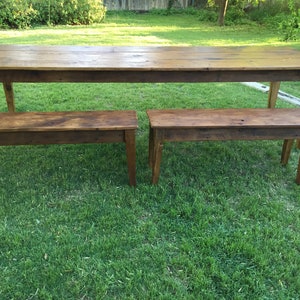 Pode incluir: Uma mesa de madeira r&uacute;stica e dois bancos colocados em um gramado verde. A mesa &eacute; longa e estreita com um acabamento de madeira natural. Os bancos s&atilde;o mais curtos e largos, tamb&eacute;m com um acabamento de madeira natural.
