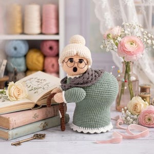 May include: A handmade crochet pincushion shaped like a grandmother, wearing glasses, a shawl, and a hat. The pincushion is green with a white lace trim. A walking stick is in her hand, and pins are stuck in her back.