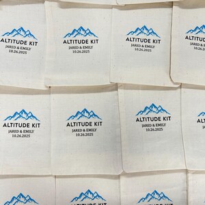 May include: Cream-coloured fabric pouches, each printed with a blue mountain design and the text "ALTITUDE KIT JARED & EMILY 10.26.2025". The pouches are arranged in a grid, ideal for event favours or gifts.