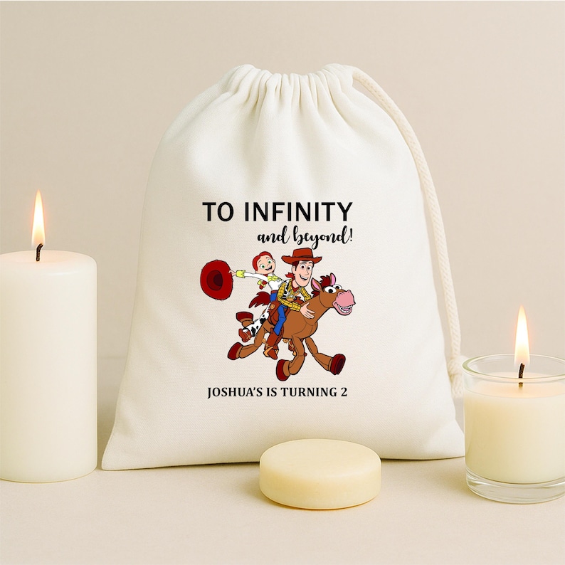 May include: A white drawstring bag with the text "TO INFINITY and beyond!" and "JOSHUA'S IS TURNING 2". The bag features a cartoon illustration of Woody and Buzz Lightyear riding a horse. Two lit candles and a small, round, light-coloured object are in the foreground.