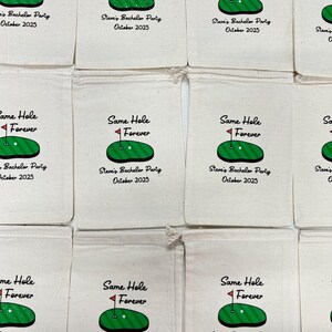May include: Cream-coloured drawstring bags, each printed with a golf course graphic and the text "Same Hole Forever." The design includes a green golf course with a red flag, and the text "Steve's Bachelor Party October 2025."