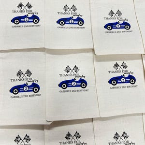May include: Cream-coloured party bags featuring a blue racing car design, chequered flags, and the text "THANKS FOR racing by" and "GABRIEL'S 2ND BIRTHDAY". The bags are laid out in a grid.