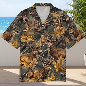 May include: Short-sleeved shirt with a camouflage design showcasing deer and autumnal leaves. The shirt has a traditional collar and a relaxed fit, suitable for casual wear. The colour scheme includes shades of brown, green, and gold.