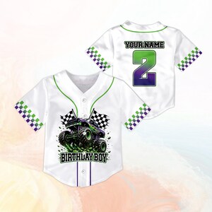 May include: White baseball jersey with green trim and a monster truck graphic. The front features the text "BIRTHDAY BOY" and the back has "YOUR NAME" above a large number 2. Checkered accents on the sleeves.