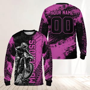 May include: A long-sleeve jersey featuring a black and pink motocross graphic. The front displays a rider on a dirt bike with the text MOTOCROSS. The back shows the text YOUR NAME and the number 00, with additional CUSTOM TEXT on the sleeves.