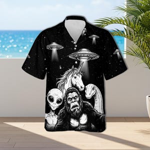 May include: Black short-sleeved button-down shirt featuring a graphic design of a unicorn, alien, gorilla, and dinosaur under UFOs against a starry background. The shirt has a classic collar and a relaxed fit, perfect for casual wear.