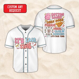 May include: A white baseball jersey with light blue trim and buttons. The front features the text IT'S FAIR TIME in pink and blue. The back displays graphics of cotton candy, corn dogs, a Ferris wheel, and blue ribbons with the text IT'S FAIR TIME.