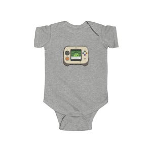 May include: A gray baby bodysuit featuring a retro handheld video game graphic. The game console is beige with colorful buttons and a green screen displaying a pixelated landscape. The bodysuit is made of soft fabric.