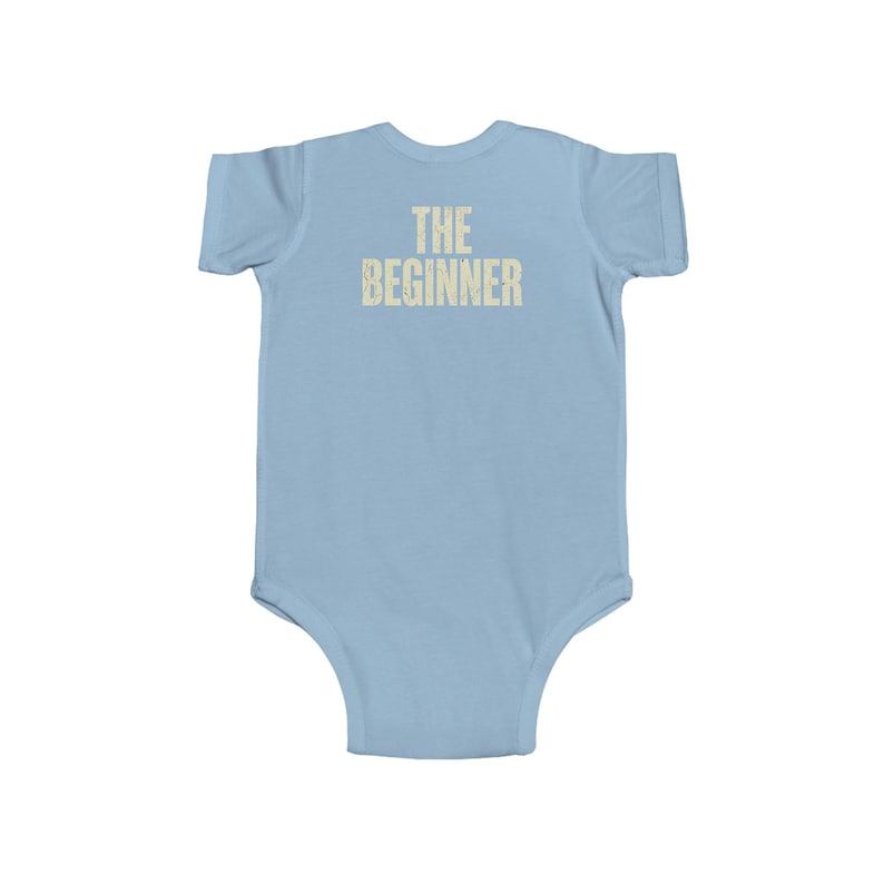May include: Light blue baby bodysuit with the text "THE BEGINNER" printed in a light beige color across the chest. The bodysuit is a one-piece garment with short sleeves and a round neckline, designed for infants.