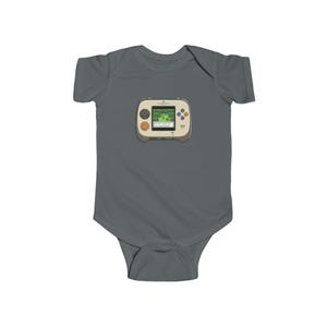 May include: A gray baby bodysuit featuring a retro handheld video game graphic. The game console is beige with colorful buttons and a green screen displaying a pixelated landscape. A fun and nostalgic design for baby apparel.