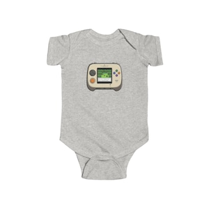 May include: A light gray baby bodysuit featuring a retro handheld video game graphic. The game console is beige with colorful buttons and a green screen displaying a pixelated landscape. The bodysuit is made of soft fabric.