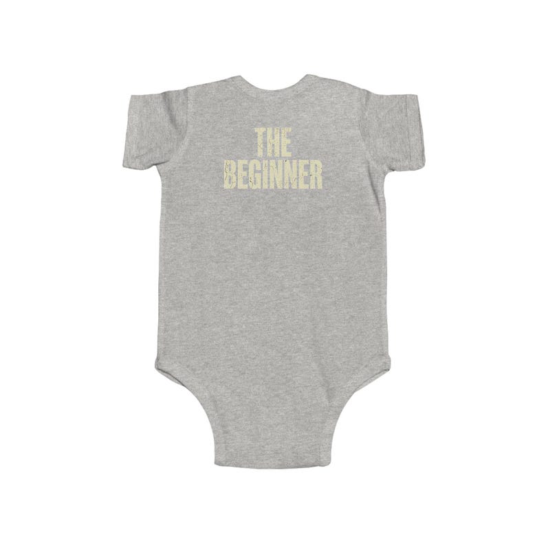 May include: A gray baby onesie with short sleeves. The text "THE BEGINNER" is printed in a light tan color across the chest. The onesie is made of a soft material and has a simple, classic design.