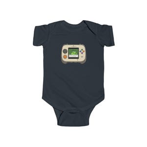 May include: A navy blue baby bodysuit featuring a retro handheld video game graphic. The game console is beige with a green screen displaying a pixelated landscape. It has orange, blue, and purple buttons.