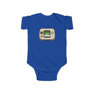 May include: A royal blue baby bodysuit featuring a graphic of a retro handheld video game console. The console is beige with a green screen displaying a pixelated game scene. It has orange and colorful buttons.