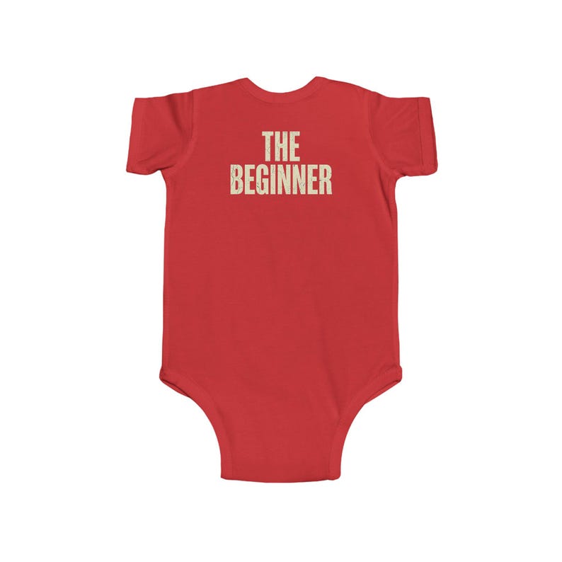 May include: A red baby bodysuit with the text "THE BEGINNER" printed in a distressed, off-white font across the back. The bodysuit is short-sleeved and has a simple, classic design.
