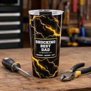 May include: A black and yellow insulated tumbler with a lightning bolt design and the text "SHOCKING BEST DAD". The tumbler is personalised with the names Brandon and Amanda-Lisa. A screwdriver and pliers are on the wooden surface.