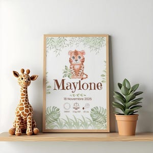 Peut inclure: Un cadre décoratif pour chambre d'enfant avec un tigre dessiné, le nom "Maylone" et des informations de naissance. Une girafe en peluche et une plante en pot sont sur une étagère en bois. L'impression comprend la date, l'heure, le poids (3 kg) et la taille (52 cm).