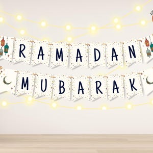 Op de afbeelding: Een feestelijke banner met de woorden "RAMADAN MUBARAK" in marineblauwe letters. De banner is versierd met gouden sterren, halve manen en kleurrijke lantaarn illustraties. Boven de banner hangt een slinger van warmwitte lichtjes.