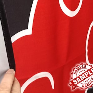 Op de afbeelding: Rode en zwarte stof met een wit wolkachtig ontwerp. De afbeelding bevat een "SAMPLE" stempel in de rechter benedenhoek. De stof is gevouwen en onthult een zwarte rand en een witte achtergrond.