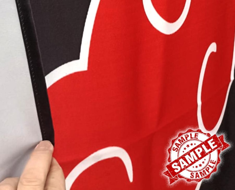 Op de afbeelding: Rode en zwarte stof met een wit wolkachtig ontwerp. De afbeelding bevat een "SAMPLE" stempel in de rechter benedenhoek. De stof is gevouwen en onthult een zwarte rand en een witte achtergrond.