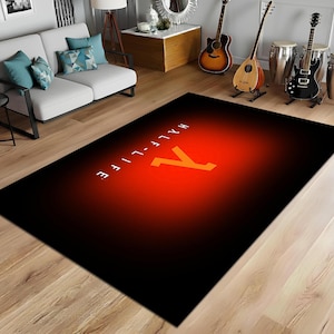 Könnte beinhalten: Ein rechteckiger schwarzer Teppich mit einem roten und orangefarbenen Farbverlauf in der Mitte. Der Teppich zeigt den Text "HALF-LIFE" in Weiß und das Lambda-Symbol in Orange. Der Teppich liegt auf einem Parkettboden.