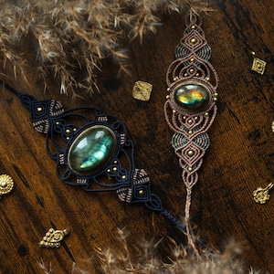 May include: Two macrame bracelets with oval, iridescent gemstones. One bracelet is navy blue with gold accents, the other is brown and teal. Small gold-colored decorative elements are scattered around.
