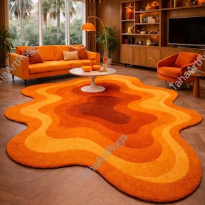 May include: An irregular, organic-shaped area rug featuring a layered, wavy pattern in shades of bright orange, burnt orange, and deep rust. The rug has a plush, textured surface and is positioned on a wooden floor in a living room.