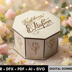 May include: A light wooden, hexagonal box with engraved floral designs and text. The box has a hinged lid with decorative script. The box is surrounded by pink and yellow flowers, suggesting a gift or decorative item.