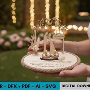 Puede incluir: Un portador de anillos de boda de madera con una silueta de pareja besándose, dos anillos y un arco decorativo. La base redonda tiene un borde de cuerda y texto. El portador lo sostiene una persona con un vestido blanco. También incluye el texto "DIGITAL DOWNLOAD".