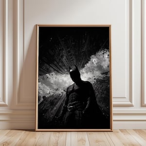 Könnte beinhalten: Schwarz-Weiß-Druck mit Rahmen, der Batman in einer Stadtlandschaft zeigt. Das Bild zeigt Batman in seinem ikonischen Anzug mit Umhang vor dem Hintergrund hoher Gebäude und bewölktem Himmel. Das Kunstwerk wird in einem Holzrahmen präsentiert.