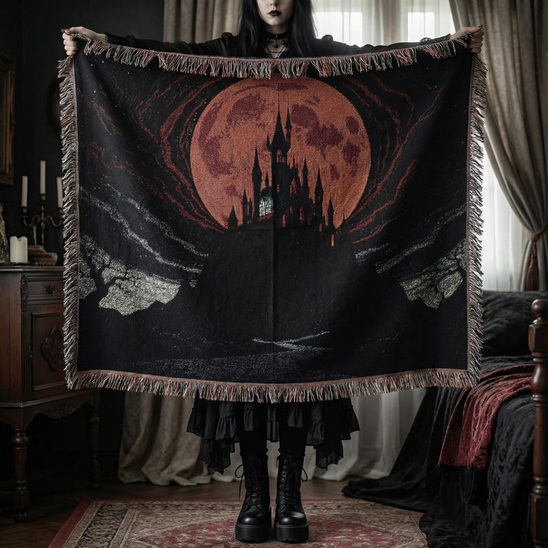 May include: Black woven throw blanket featuring a gothic castle silhouette under a large red moon. The blanket has a fringed edge and a dark, dramatic aesthetic. The design evokes a spooky, fantasy theme.
