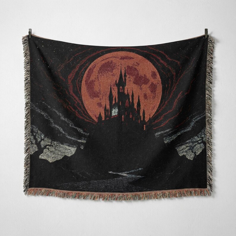 May include: Black throw blanket featuring a gothic castle silhouette against a large, reddish-orange full moon. The design includes a dark night sky with stars and a river. The blanket has a fringed edge.