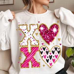 May include: White sweatshirt with a large "XO" design and two hearts. The "X"s are outlined in gold glitter, one with a pink zebra print and the other with a white polka dot pattern. The hearts are pink and black with gold glitter accents.
