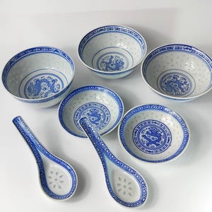 May include: A collection of six white porcelain bowls and spoons with blue dragon and geometric patterns. The bowls feature a perforated rim design. The spoons have a floral pattern in the bowl.