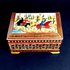 May include: A rectangular wooden box featuring a hand-painted lid depicting two figures on horseback in a landscape. The sides of the box are decorated with intricate geometric marquetry patterns in shades of brown, black, and cream.