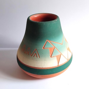 May include: A rounded ceramic vase featuring a gradient color scheme that transitions from deep green at the top to a lighter cream shade, accented by a terracotta orange base and rim. The surface displays carved geometric patterns throughout.