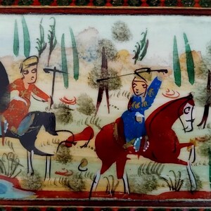 May include: A rectangular decorative box featuring a hand-painted scene of two figures on horseback. One figure wears a red garment on a black horse, while the other wears a blue garment on a red horse. The background depicts trees and a small blue pond.